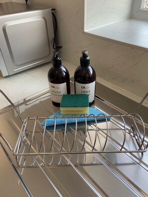 A kitchen with a dish rack holding a blue cloth and a sponge, and two bottles of hand sanitizer and dish soap on the counter.