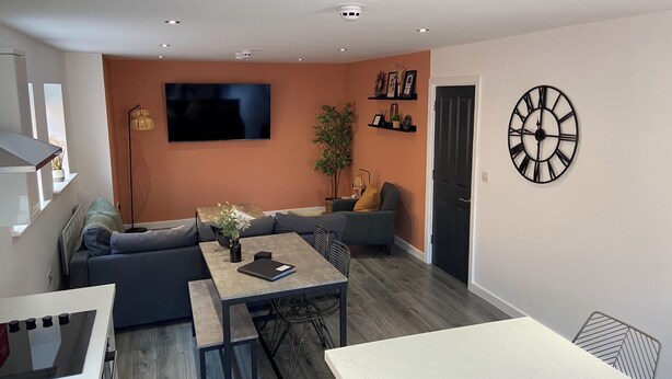 A modern living room with a sofa, a dining table, and a TV mounted on the wall.