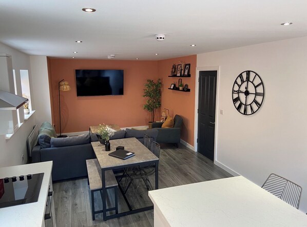 A modern living room with a sofa, a dining table, and a TV mounted on the wall.