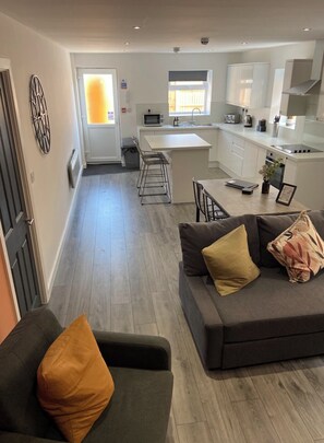 A modern kitchen with white cabinets, a central island, and a dining area with a grey sofa and a coffee table.
