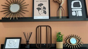 Two black shelves against a peach wall, each holding various decorative items including framed artwork, a mirror, and a potted plant.
