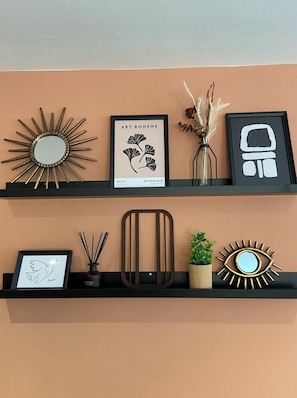 Two black shelves against a peach wall, each holding various decorative items including framed artwork, a mirror, and a potted plant.