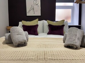 A bedroom with a bed, pillows, a blanket, and a wall art piece.