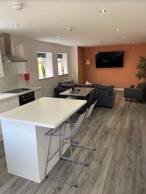 A modern kitchen with a central island, a dining area with a sofa, and a flat-screen TV mounted on the wall. - The Gateway Apartment 1 (Blackpool)
