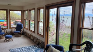 A room with large windows overlooking a lake, wicker chairs, a patterned rug, and a view of colorful kayaks outside. - Gorgeous, sweeping views of Lake Tahoe from 3 story lake front condo! (Tahoe City)