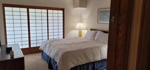Un dormitorio con cama, una mesita de noche con lámpara, un escritorio de madera y una puerta corredera de estilo japonés.