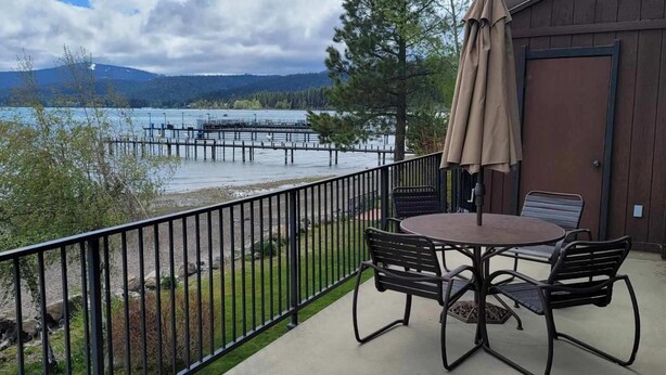 A balcony with a table and chairs overlooking a lake, a wooden building, and a metal railing. - Gorgeous, sweeping views of Lake Tahoe from 3 story lake front condo! (Tahoe City)
