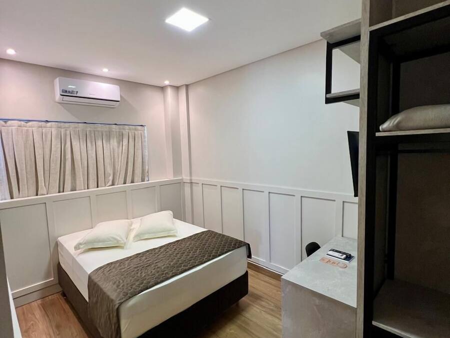 Un dormitorio con cama, escritorio, silla, unidad de aire acondicionado y ventana con cortinas.