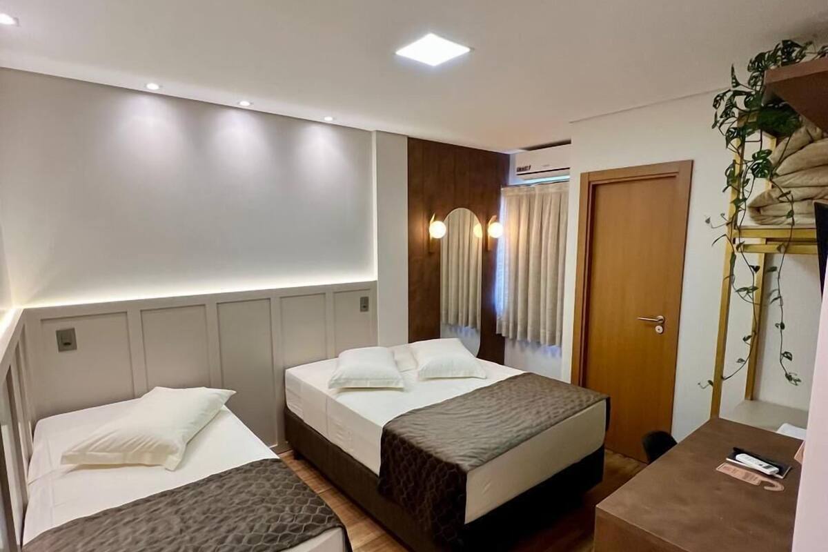 Una habitación de hotel con dos camas, piso de madera, un escritorio y un espejo.