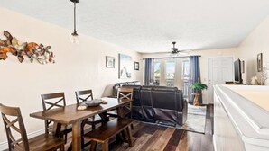 Un coin repas avec une table et des chaises en bois, un ventilateur de plafond et une vue sur l’extérieur grâce à une porte coulissante.