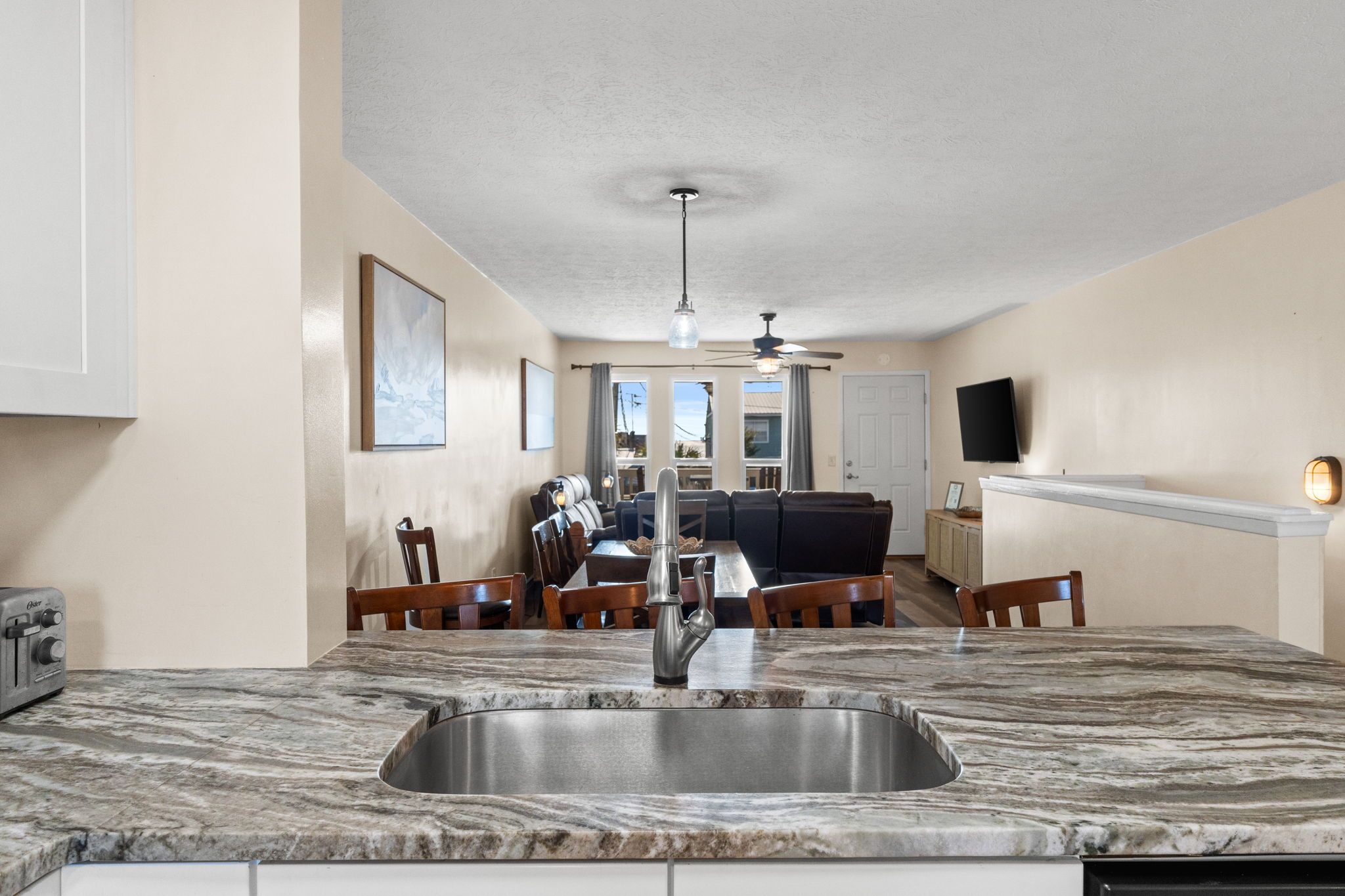 A kitchen with a marble countertop, a stainless steel sink, wooden chairs, and a dining table.