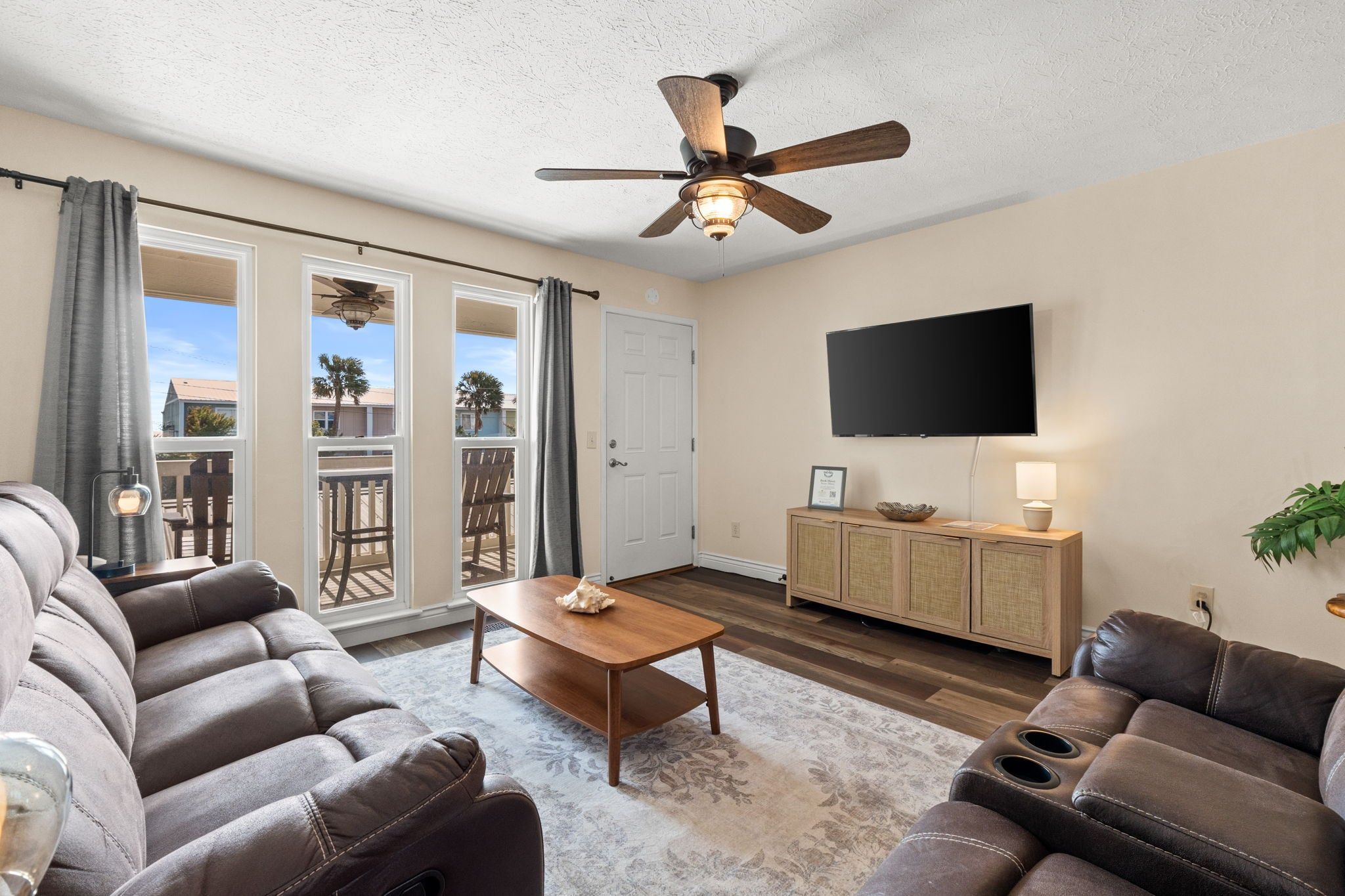A living room with a ceiling fan, a flat-screen TV, a wooden coffee table, and leather sofas.