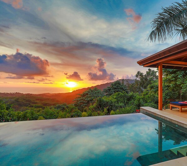 A poolside area with a view of the sunset and hills.