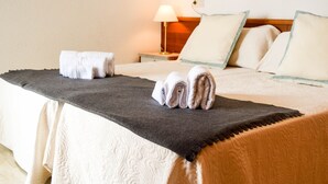 A neatly made bed with a dark headboard, a bedside table with a lamp, and a wall socket.