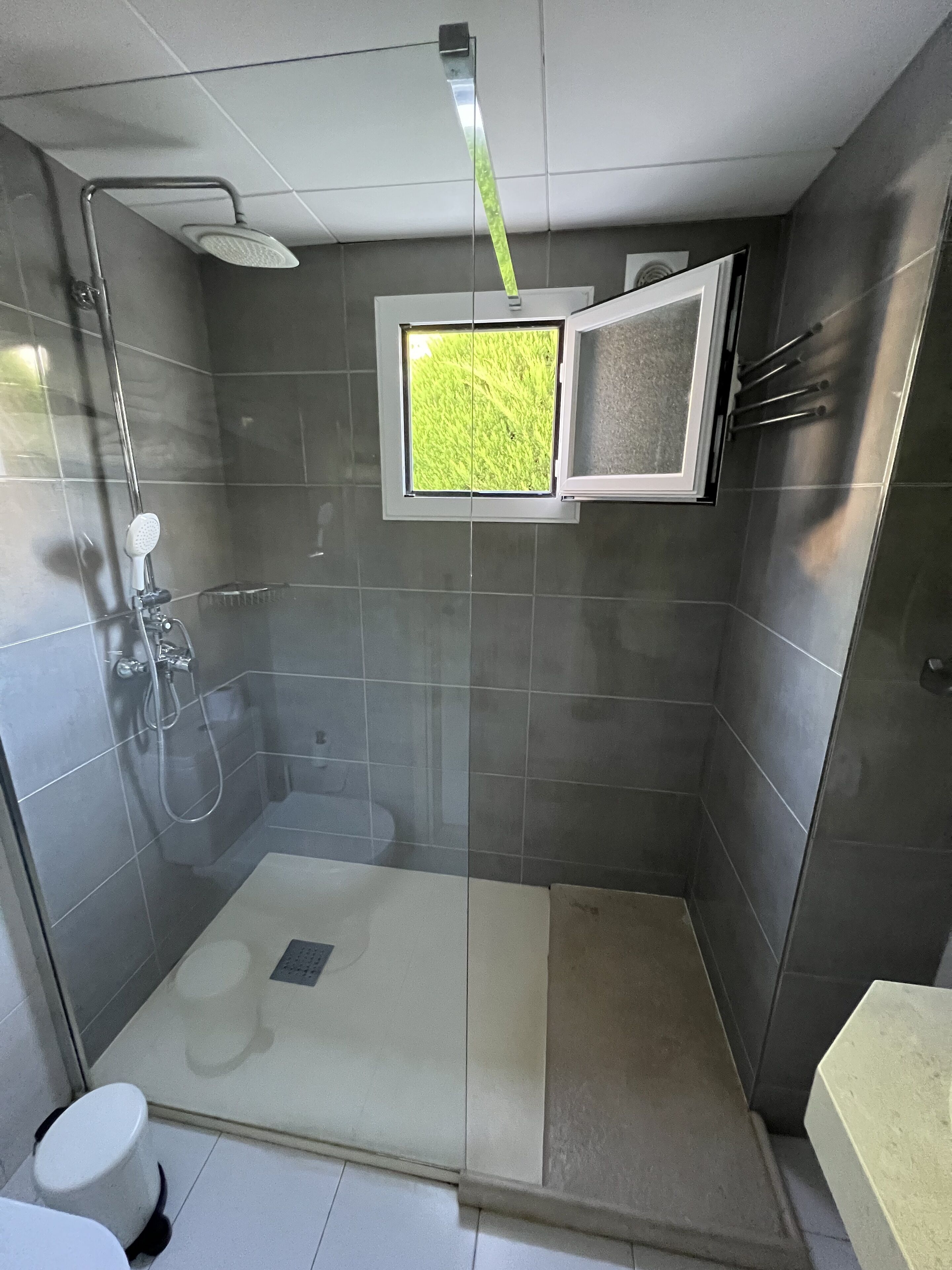 Et lille, aflukket bruseområde med et vindue, et toilet og en vask.