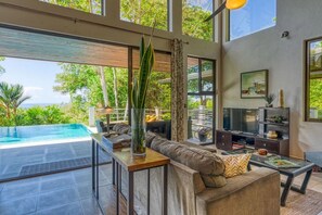 Una sala de estar moderna con un ventanal grande, piscina y vistas a la vegetación.