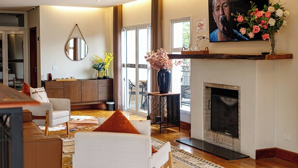 Una sala de estar con chimenea, un televisor montado encima y un comedor visible a través de puertas de vidrio.