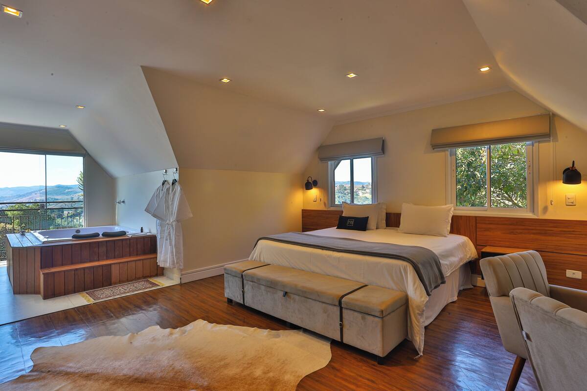 Un dormitorio con una cama grande, una sala de estar, una bañera y vistas al exterior.