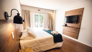 Habitación de hotel con cama, suelo de madera, televisor montado en la pared y ventana con cortinas.