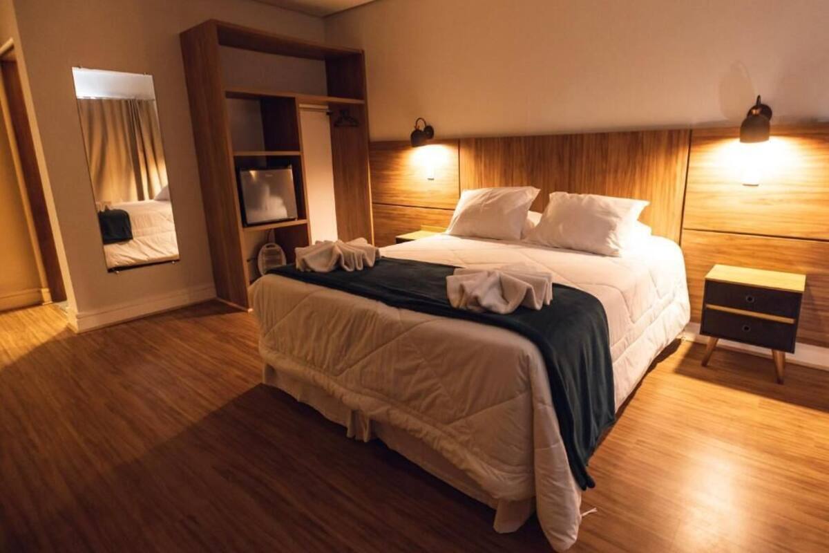 Habitación de hotel con una cama grande, cabecero de madera, mesitas de noche, un armario y un espejo.