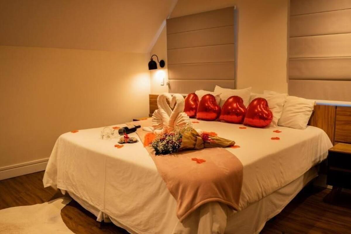 Una cama bien hecha con una colcha blanca, almohadas rojas y un ramo de flores.