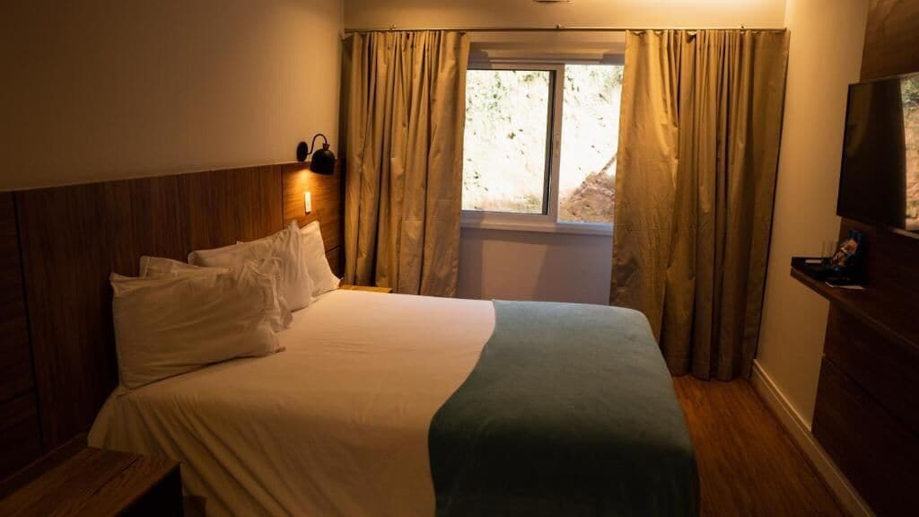 Ein Hotelzimmer mit Bett, Nachttisch, Fernseher und einem Fenster mit Vorhängen.