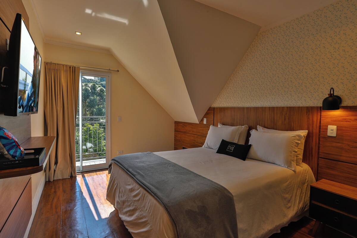 Un dormitorio con una cama grande, cabecera de madera, televisor montado en la pared y un balcón con cortinas.