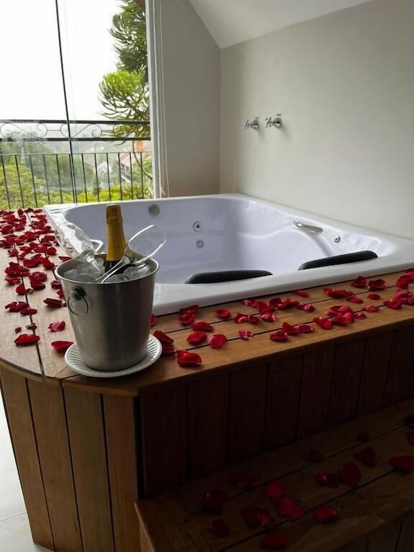 Zona de spa con una bañera grande, un cubo con una botella y pétalos de rosa esparcidos sobre el banco de madera.