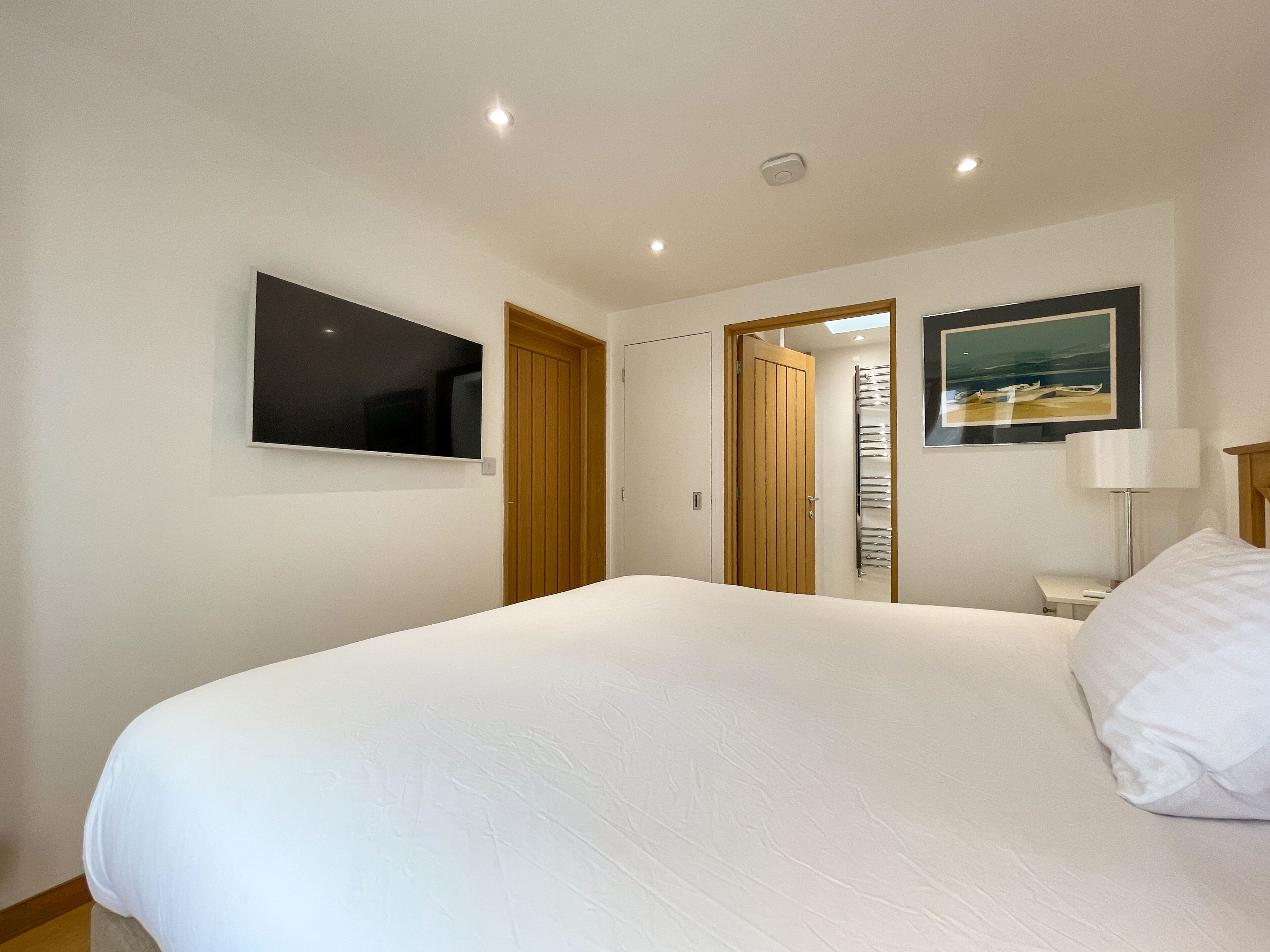 Camera d'albergo con un letto grande, una TV a muro, un quadro e una lampada.