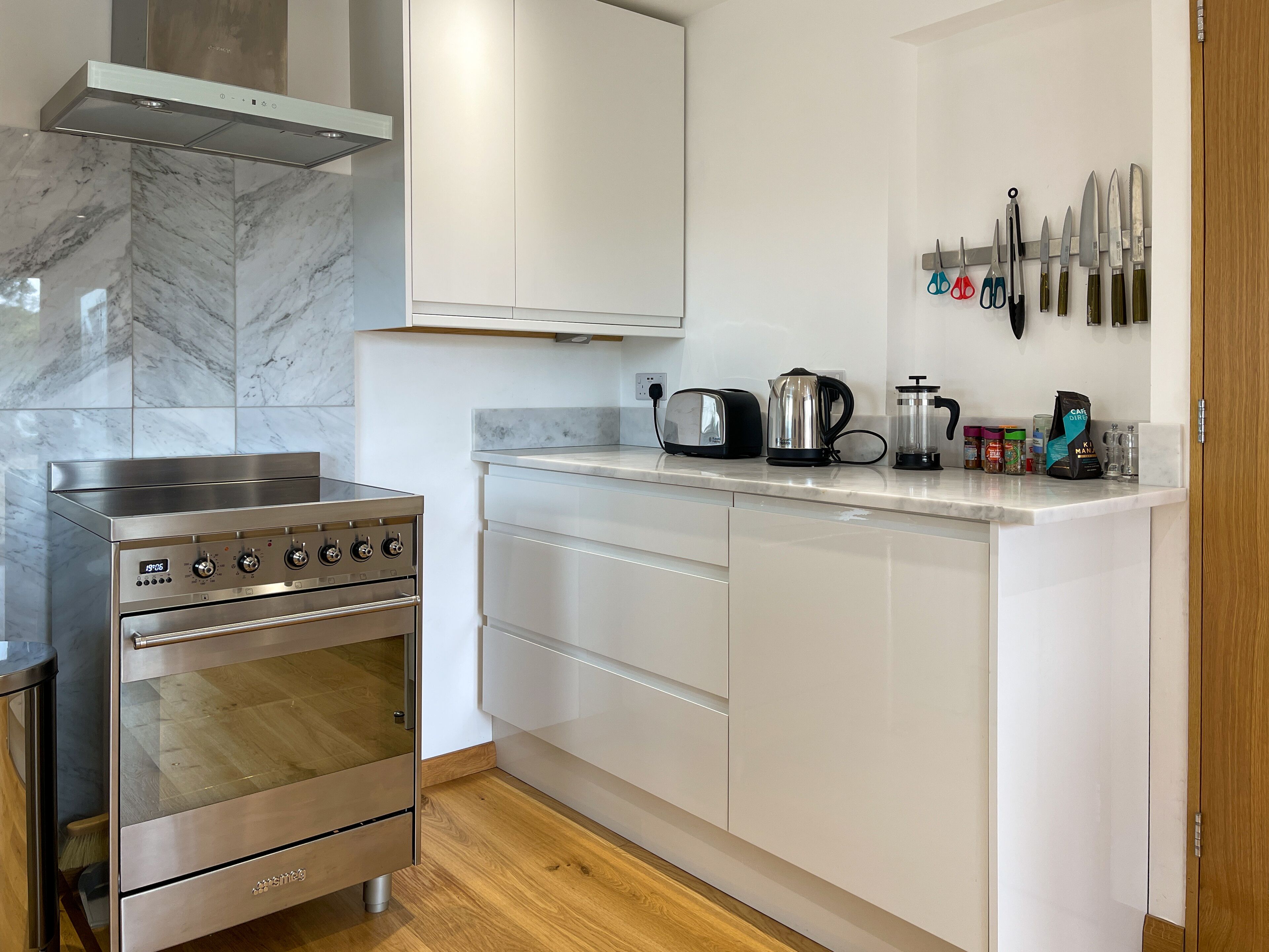 Una cocina moderna con estufa de acero inoxidable, armarios blancos y salpicadero de mármol.