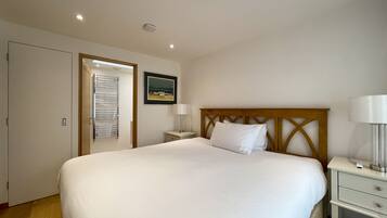 A neatly arranged bedroom with a large bed, a bedside table with a lamp, a small bedside table with a lamp, and a framed picture on the wall.