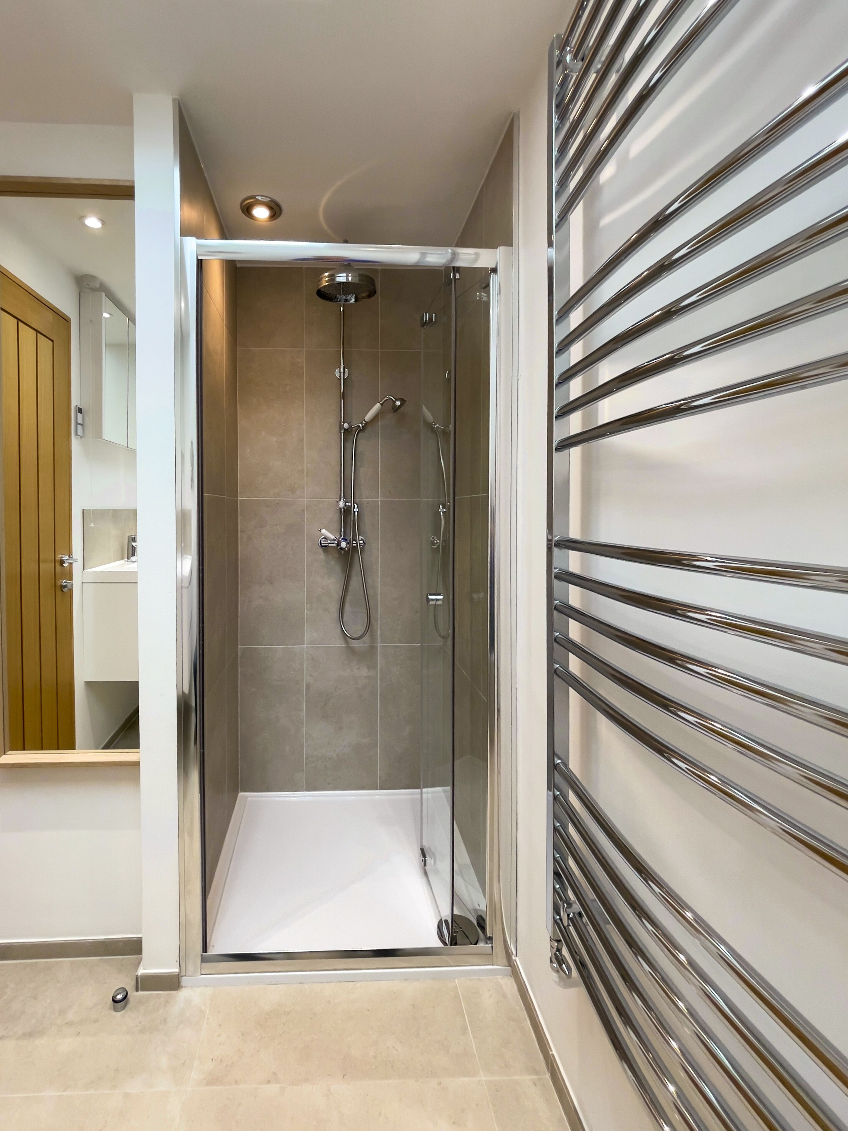 Un espace douche moderne doté d’une porte en verre, d’un pommeau de douche et d’un pommeau de douche à main.