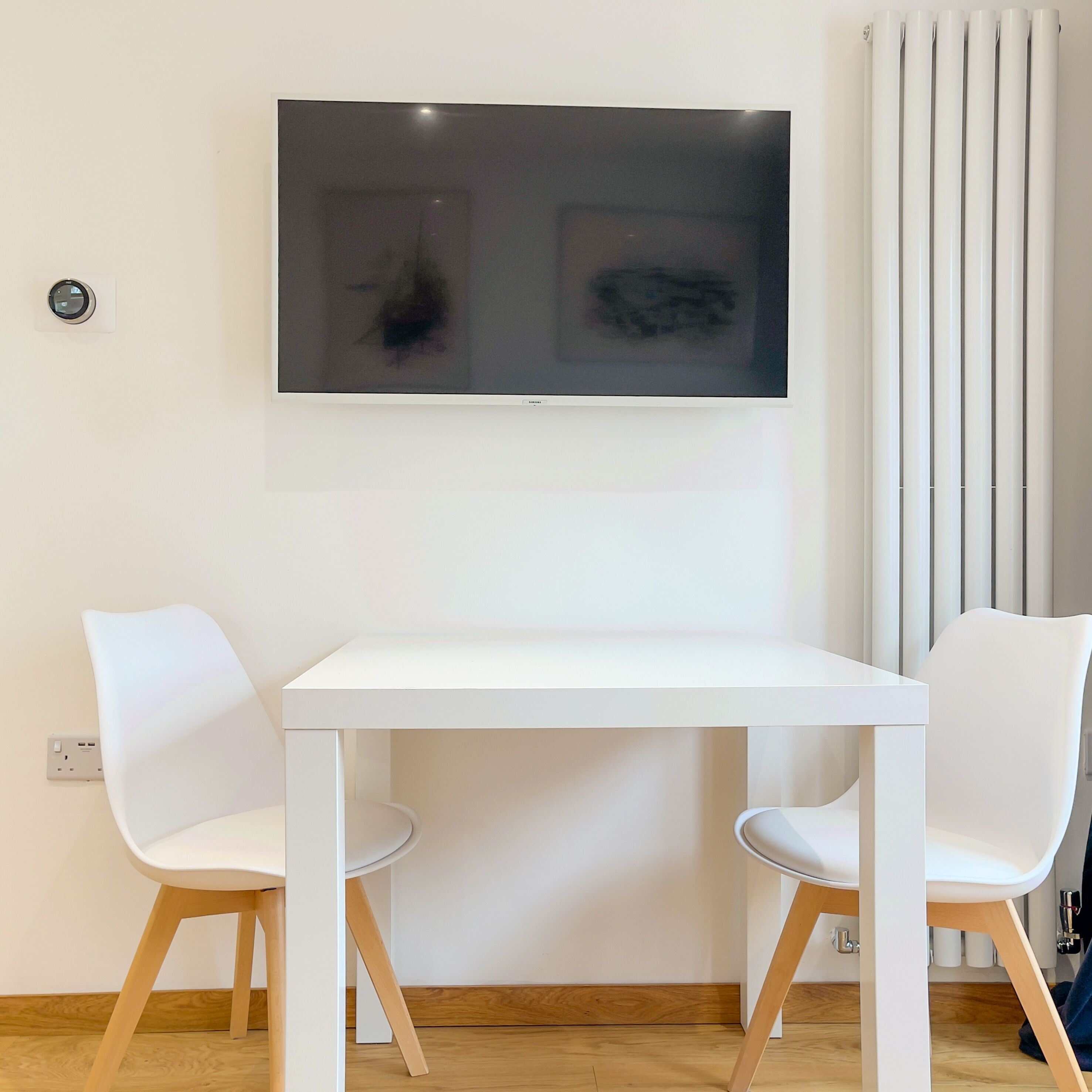 A modern room with a white table and two white chairs, a large abstract painting on the wall, and a radiator.