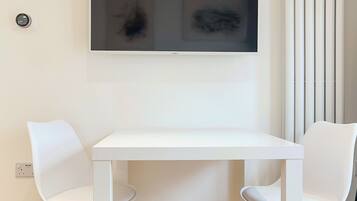A modern room with a white table and two white chairs, a large abstract painting on the wall, and a radiator.