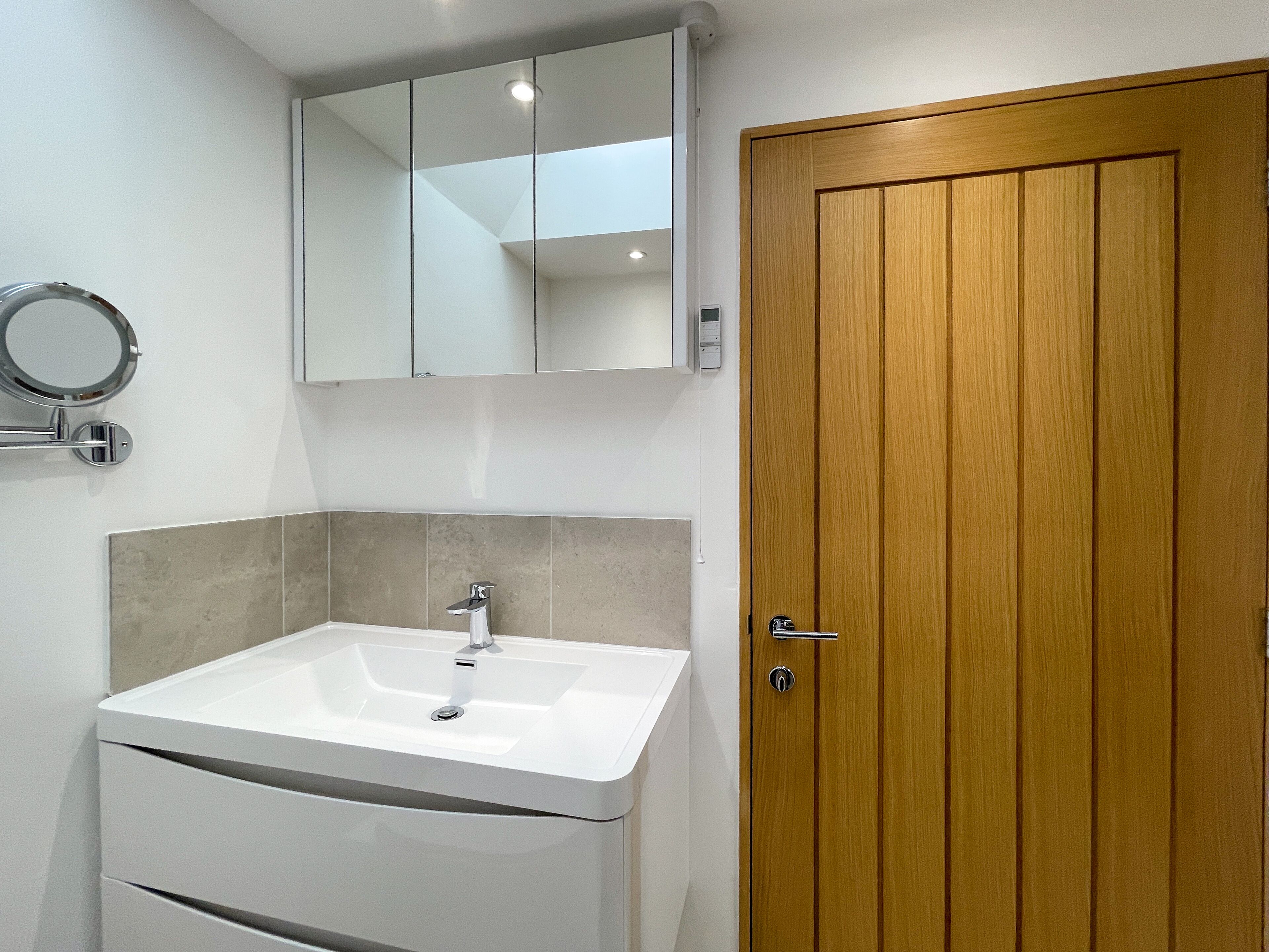 Een badkamer met een witte wastafel, een houten deur en een spiegel boven de wastafel.