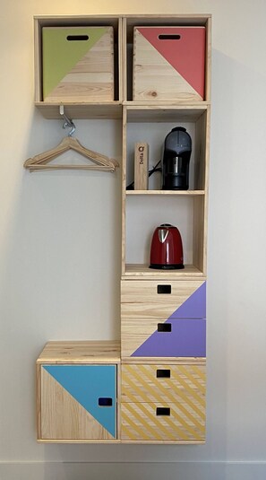Un mueble de almacenamiento de madera con varios compartimentos, incluyendo una cafetera y un hervidor rojo.