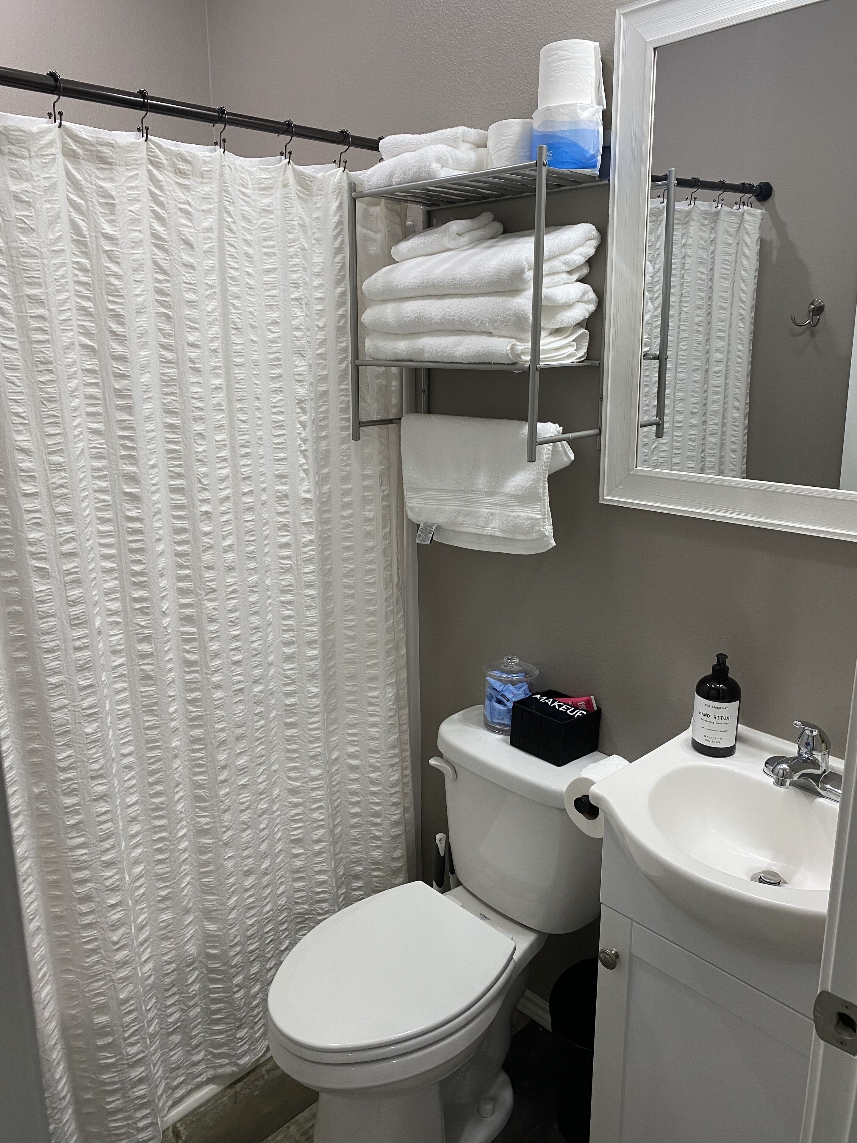 A bathroom with a white toilet, a sink, a towel rack with folded towels, and a shower curtain.