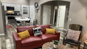 A living room with a red leather sofa, a coffee table, and a dining area with a white table and chairs. - Cozy Cottage in Rayburn Country-Pet Friendly-King Suite/Pool Table! Sleeps 10 (Brookeland)