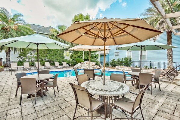 Une terrasse extérieure avec une piscine, entourée de chaises longues et de parasols.