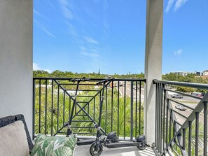 Ein Balkon mit Blick auf eine Straße und Grünflächen, einem Metallgeländer und einem Roller.