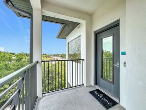 A balcony with a metal railing, a door with a keypad lock, and a welcome mat.