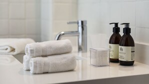 Un baño con un lavabo blanco, dos botellas de loción y toallas dobladas con cuidado.