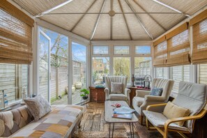 Ein Wintergarten mit Holzboden, einer Couch, zwei Sesseln und einem Couchtisch.