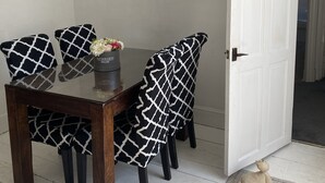 A dining area with a dark wooden table and chairs with a black and white pattern. There is a vase with flowers on the table. - Stunning 2-bed Apartment Above Schooners Bar (Neath)