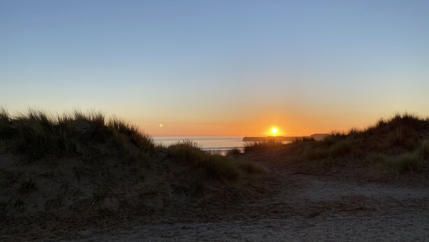 A beach scene with a sunset, sand dunes, and a distant pier. - Stunning 2-bed Apartment Above Schooners Bar (Neath)