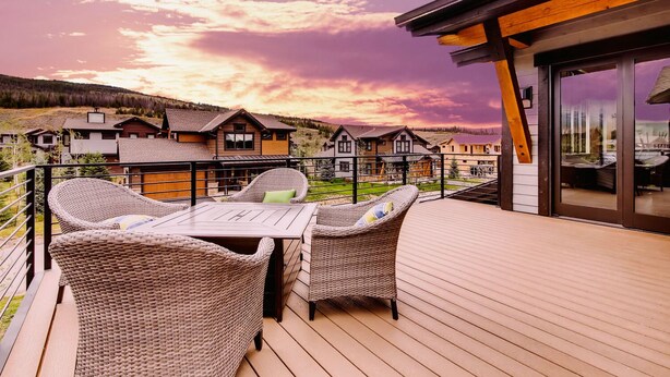 Eine Terrasse mit Korbmöbeln und einem Tisch, mit Blick auf eine Wohngegend mit Häusern und einem See.