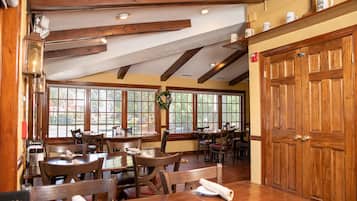A restaurant with wooden tables and chairs, large windows, and a wooden door.