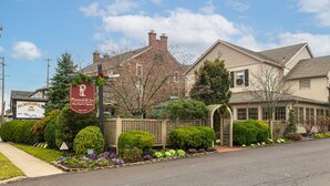 Um edifício de dois andares com fachada de tijolos, um letreiro do Plumsteadville Inn, e um jardim bem cuidado com diversas plantas e flores.