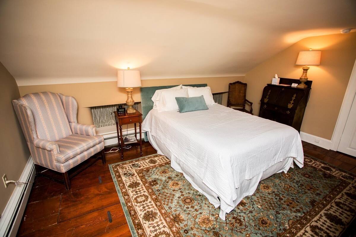 A bedroom with a bed, a chair, a nightstand, a lamp, and a patterned rug.