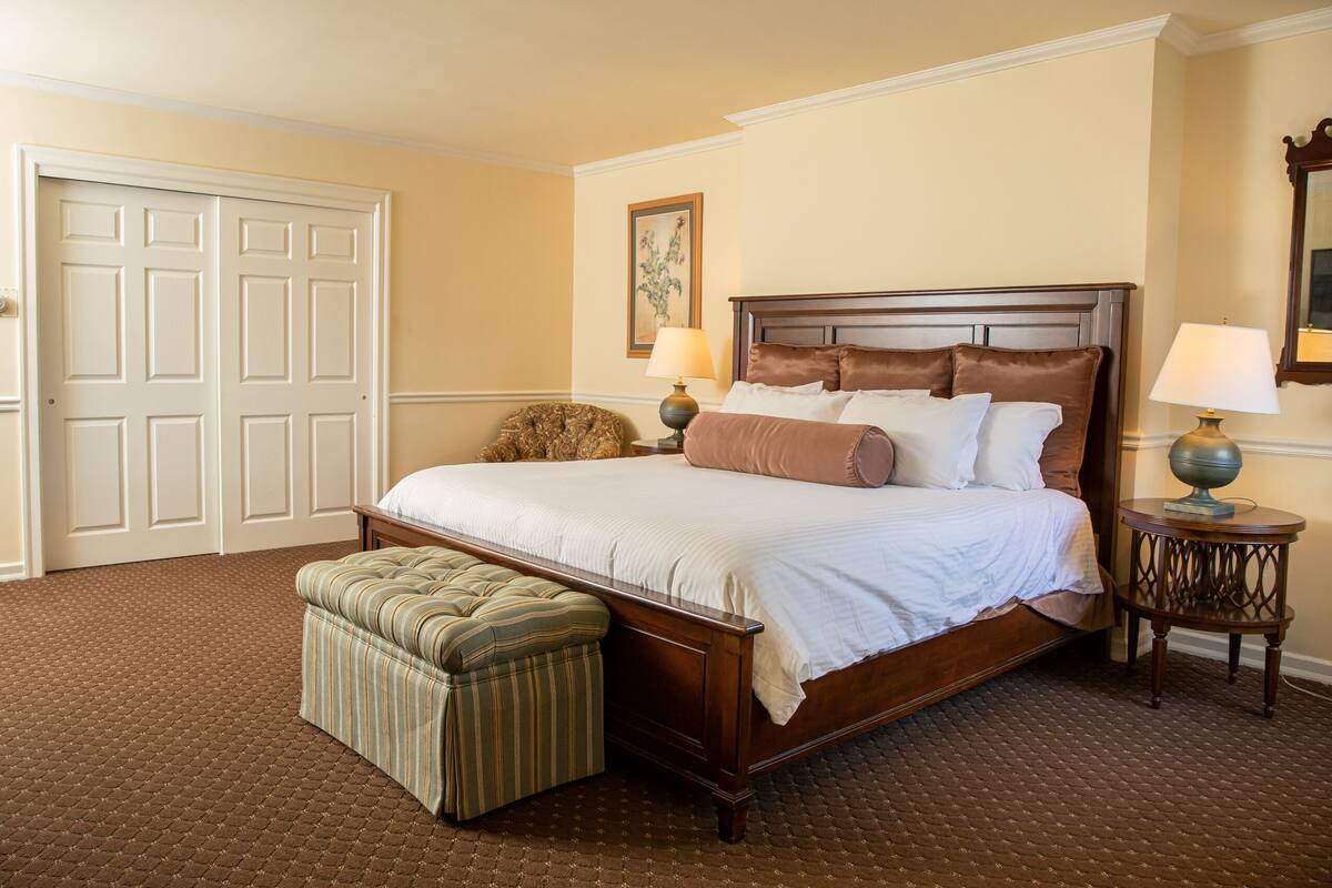 A bedroom with a large bed, a matching bench, two bedside tables, and a door.